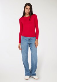 Czerwona bluzka z długim rękawem połączona z luźnymi, jasnoniebieskimi dżinsami. Bluzka ma okrągły dekolt; dżinsy mają lekki rozszerzany krój przy nogawkach.