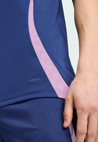 Mornarska atletska majica s ružičastom teksturiranom prugom, napravljena od tkanine koja odvodi vlagu. Sadrži "ClimaCool" logo na rubu.