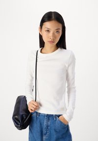 Maglietta bianca a maniche lunghe con collo rotondo, abbinata a pantaloni corti in denim a vita alta e una borsa a spalla nera.