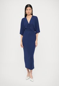 Laivastonsininen midi-mekko, jossa on kiristysnauha, leveät hihat ja istuva siluetti. Sileä kangas ja nilkkapituinen malli.