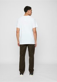 Camiseta blanca de manga corta combinada con pantalones rectos marrones y zapatillas negras. El conjunto es sencillo, con un ajuste relajado y un diseño minimalista.