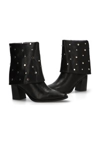 Botas de tobillo de cuero negro con un upper plegado que presenta tachuelas metálicas plateadas. Diseño de punta afilada y tacón grueso. Textura suave.
