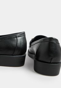 Schwarze Lederschuhe mit glatter Oberfläche, runder Zehenform, niedrigem Absatz und Nähdetails an der Rückseite. Subtiler Glanz auf dem Material.