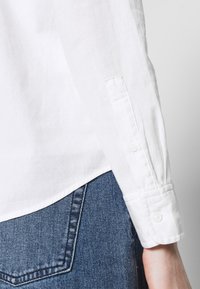 Vit linneskjorta med knäppta manschetter, med en mjuk textur och rundad nederkant, i kombination med blå denimjeans.