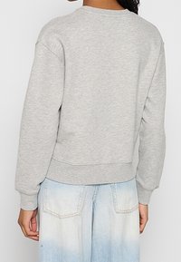 Sudadera gris de manga larga, con cuello redondo, puños y bajo acanalados. Combinada con vaqueros anchos azul claro ligeramente desgastados.