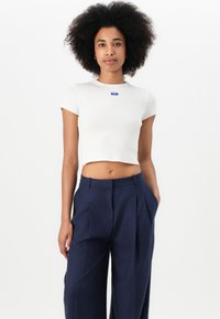 Vit räfflad kort t-shirt med en blå logotyp på bröstet, i kombination med marinblå högmidjade byxor med lös passform och vida ben.