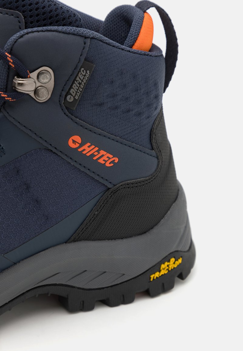 Scarpa da trekking impermeabile in blu navy e nero con tessuto texturizzato, dettagli arancioni e suola in gomma robusta con caratteristiche di grip e trazione.