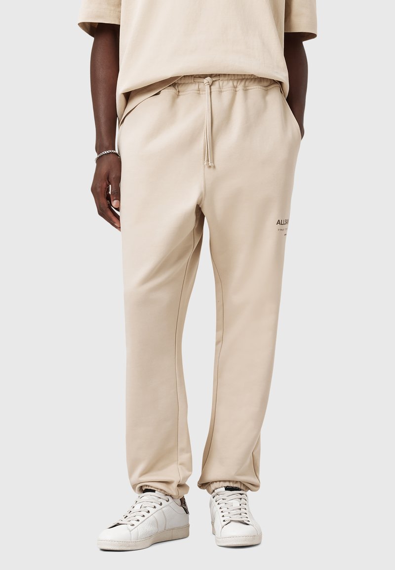 Beige sweatpants lavet af blødt stof, med elastisk talje og snøre, sidelommer og et lille brandlogo på låret.