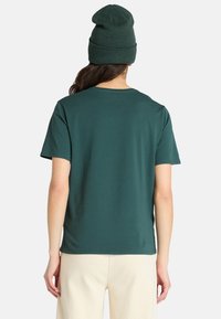 Kortærmet, tætsiddende t-shirt i mørkegrønt bomuld med rund halsudskæring og glat tekstur. Båret med en matchende beanie.