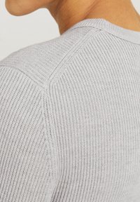 Pull en maille côtelée gris clair avec un col rond et des manches raglan, présentant une texture douce et un motif texturé.
