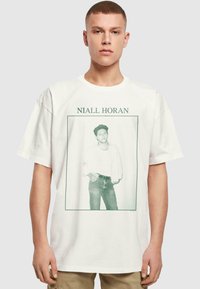 Hvit bomull t-skjorte med grønn grafisk trykk av en figur i en ramme med tekstene "Niall Horan" over. Avslappet passform og korte ermer.