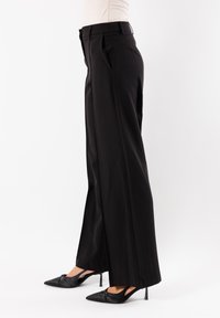 Pantaloni neri a gamba larga con pieghe, realizzati in tessuto morbido. Abbinati a tacchi alti neri a punta, creano una silhouette elegante.