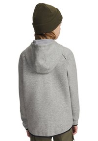 Grijze hoodie met een zachte textuur, lange mouwen en een ronde zoom. Draagt een olijfgroene gebreide beanie.
