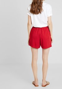 Pantalones cortos ligeros rojos con cintura elástica, textura suave y un corte holgado, combinados con una camiseta blanca y sandalias.