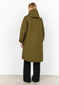 Olive green quilted long coat with a hood; features a woven texture, side zip, and a relaxed fit, paired with black wide-leg pants.