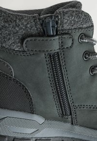 Bottine noire en gris foncé avec accent en feutre, surface synthétique lisse, détail de fermeture éclair et semelle texturée pour une meilleure adhérence. Présente des coutures renforcées.