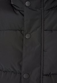 Černá zateplená bunda s hladkým, matným povrchem, která má kulaté černé knoflíky a prošívané části pro izolaci.
