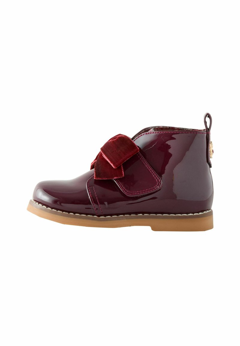 Glänzende kastanienbraune Lackleder-Boots mit einem roten Samtbogen, einer hellbraunen Gummisohle und dekorativen Nähten entlang der Kante.
