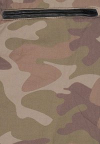 Primissimo piano di un tessuto con un motivo camouflage beige, verde e marrone, dotato di una tasca a zip orizzontale nera nella parte superiore.