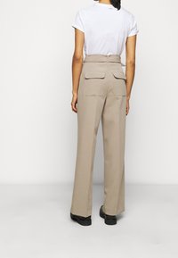 Pantalons beige à jambes larges avec deux poches arrière, taille haute et design ajusté. Associés à un t-shirt blanc à manches courtes.
