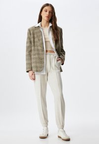 Geruite blazer in beige en bruin, oversized pasvorm. Witte blouse met kleur, cropped beige top, lichtgrijze joggingbroek, witte sneakers.