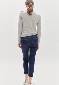 Suéter gris claro combinado con jeans ajustados azul oscuro. Los jeans tienen dos bolsillos traseros y puños enrollados. Zapatillas blancas completan el atuendo.