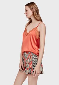 Satin-Orange-Camisole mit Spitzenrand, kombiniert mit gemusterten Shorts, die florale und geometrische Designs in Rot, Schwarz und Weiß aufweisen.