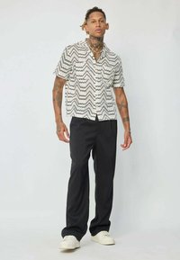 Chemise à manches courtes noire et blanche à motifs avec des designs en zigzag, associée à un pantalon noir et des baskets blanches. Style décontracté, coupe ample.