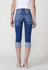 Jean capri en denim bleu moyen avec une finition légèrement délavée. Comprend des ourlets brodés, deux poches arrière et une étiquette en cuir de marque.