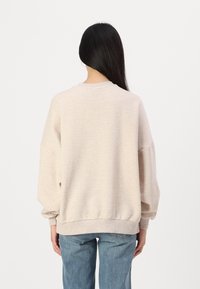 Felpa oversized beige con polsini e orlo a coste, realizzata in morbido tessuto, caratterizzata da un classico scollo rotondo e spalle scese.