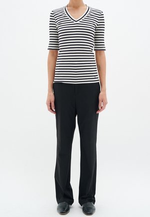 Mustat ja valkoiset raidalliset, ribbed V-kaula-aukkoinen paita lyhyillä hihoilla, yhdistetty mustiin suoriin housuihin ja mustiin kenkiin.