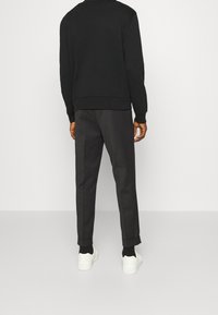 Felpa nera con polsini e orlo a costine, abbinata a pantaloni grigi scuri con vestibilità su misura. Sneakers bianche completano l'outfit.