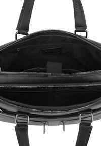 Black leather bag interior with zippered compartments, textured surface, and silver hardware accents. Multiple storage pockets visible.