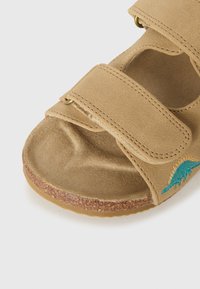 Sandale din piele întoarsă de culoare bej, cu două curele cu închidere velcro, vârf rotund, talpă texturată și broderie decorativă turcoaz pe lateral.