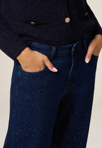 Jeans in denim blu navy con un motivo di decorazione in pietre, dal taglio classico, con tasche laterali e una texture morbida.
