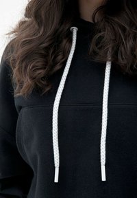Czarna bluza z kapturem z kangurzym kieszonką, białymi sznurkami ściągającymi i fakturowanym materiałem. Projekt obejmuje proste szwy oraz elastyczne mankiety.