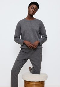 Grau gequiltetes Lounge-Set mit einem langärmeligen Oberteil mit Rundhalsausschnitt und tapered Hosen, gefertigt aus strukturiertem Stoff.