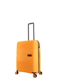 Hard-shell orange suitcase with vertical grooves, black retractable handle, and four multicolored wheels. Features a logo patch on the front.