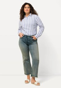 Camisa blanca de botones con Rayas verticales azules, combinada con jeans azules de tiro medio, ligeramente acampanados y sandalias blancas con un diseño anudado.
