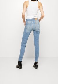 Jeans ajustados de color azul claro con una cintura alta, cinco bolsillos y una etiqueta de cuero en la parte posterior de la cintura. Modelo llevando botas negras hasta el tobillo.