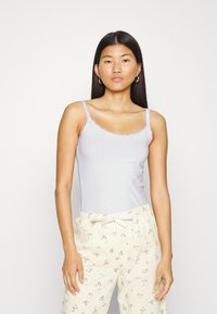 Camisola lilla chiaro con bordo in pizzo, caratterizzata da spalline sottili. Indossata con pantaloni da pigiama a fiori giallo chiaro. Tessuto morbido.