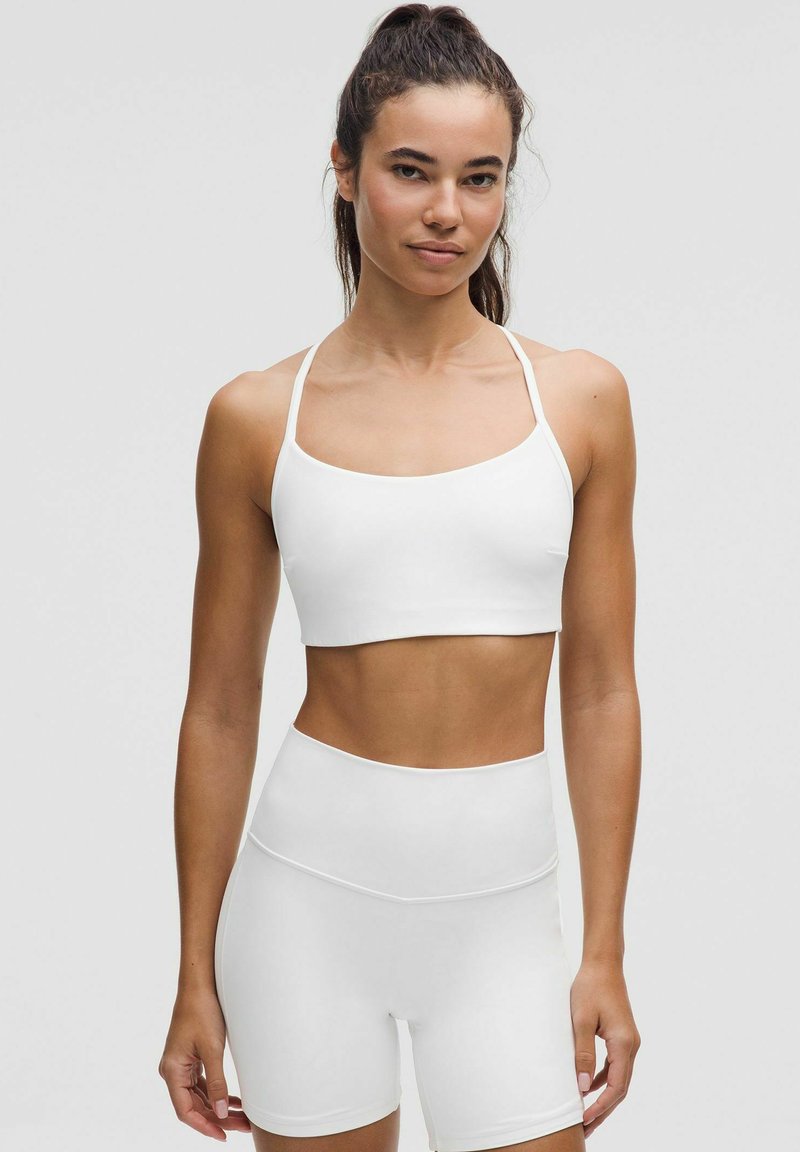 Weißes sportliches Crop-Top und hochgeschnittene Shorts aus elastischem Material, mit minimalistischem Design und glatter Textur.