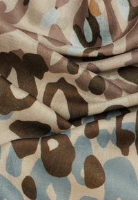Fabric with abstract animal print in beige, brown, and light blue, showing folds and texture of the textile material.