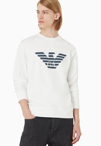 Felpa bianca con colletto a girocollo, caratterizzata da un logo aquila a strisce orizzontali blu scuro sul petto. Vestibilità slim, polsini e orlo a coste.