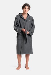 Šedý kapucínský plášť s vázáním v pase, vyrobený z měkké látky. Má na rukávu branding "arena" a texturovaný design na lemu.