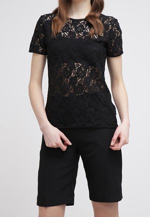 Schwarzes Spitzenoberteil mit floralem Muster und kurzen Ärmeln, kombiniert mit schwarzen Shorts. Die Spitze hat ein zartes, strukturiertes Aussehen.