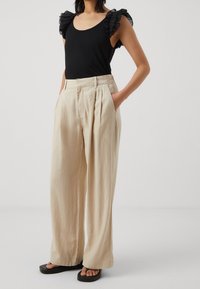 Svart linne med volangärmar, beige vida byxor med veck och svarta sandaler. Svala material och neutrala färger.