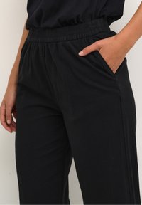 Černé kalhoty s elastickým pasem a bočními kapsami, charakterizovan�é volným střihem a měkkou, texturovanou tkaninou, viditelnými švy a celkovým uvolněným designem.