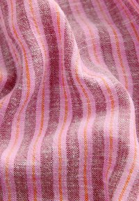 Gros plan d'un tissu tissé avec des rayures verticales roses, violettes et orange, montrant une texture détaillée et des plis doux.