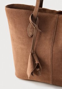 Καφέ τσάντα tote από σουέντ με απαλή υφή, διαθέτει απλό σχέδιο, ραφές ως διακοσμητικά στοιχεία και λουρί με κόμπο.